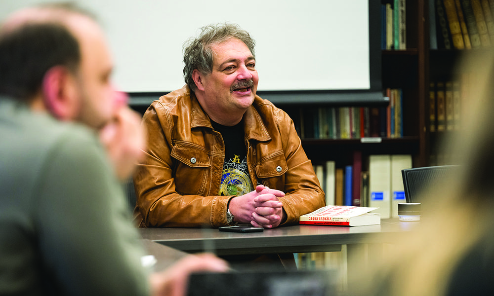 Bykov smiling while seated at seminar table with students seated around him.