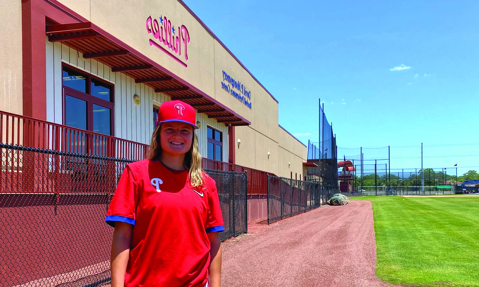 Beth Greenwood, wearing a Philadelphia Phillies hat and T-shirt stands beside a team training center.