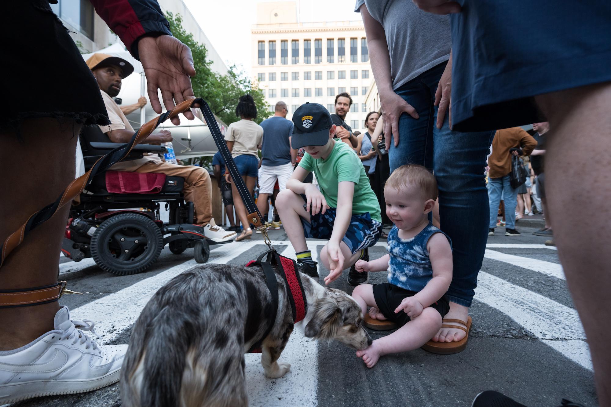 A baby and a small child are pictured with a tiny dog outside among a crowd of people